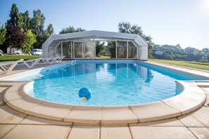 A swimming pool with a covered area, a tiled deck, and a clear blue sky. - Auberge du Pastel (Nailloux)