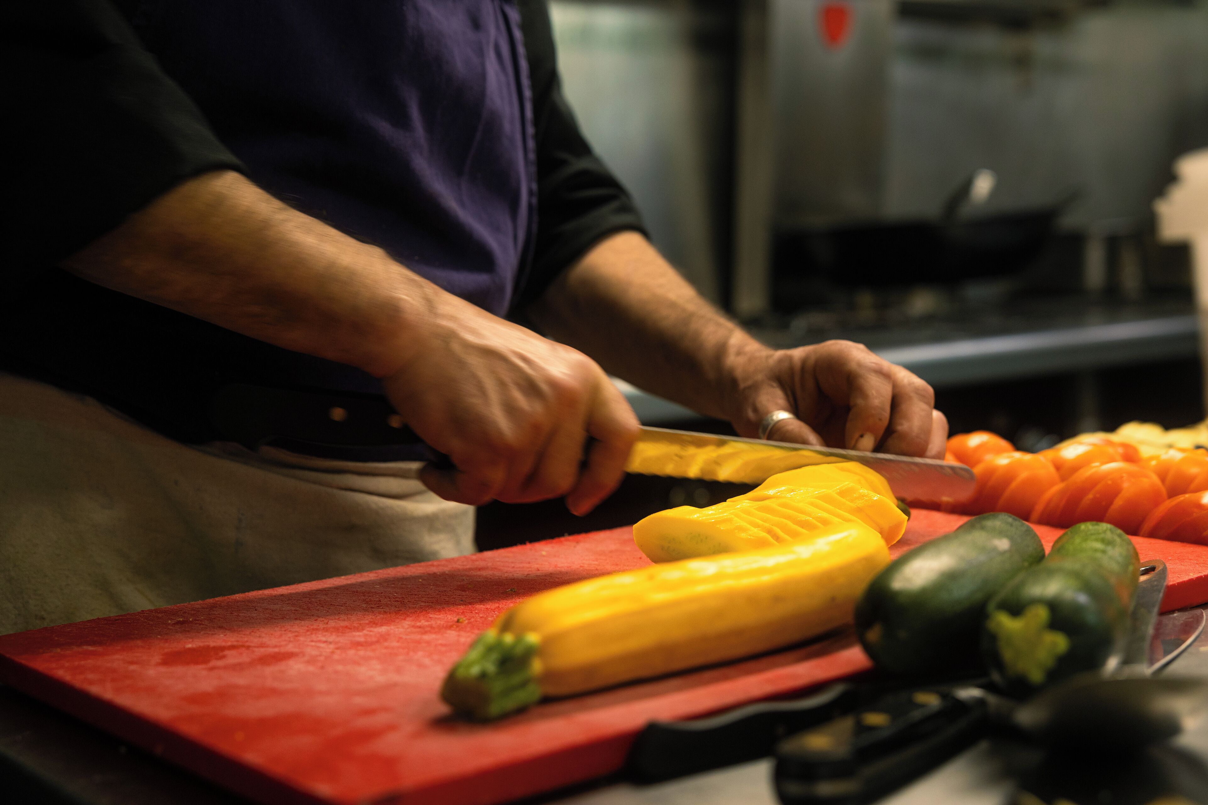 En person skærer grøntsager på en rød skærebræt.