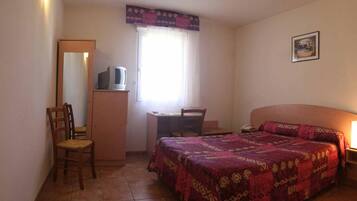 A bedroom with a bed, a desk, a chair, a television on a cabinet, and a window with curtains.