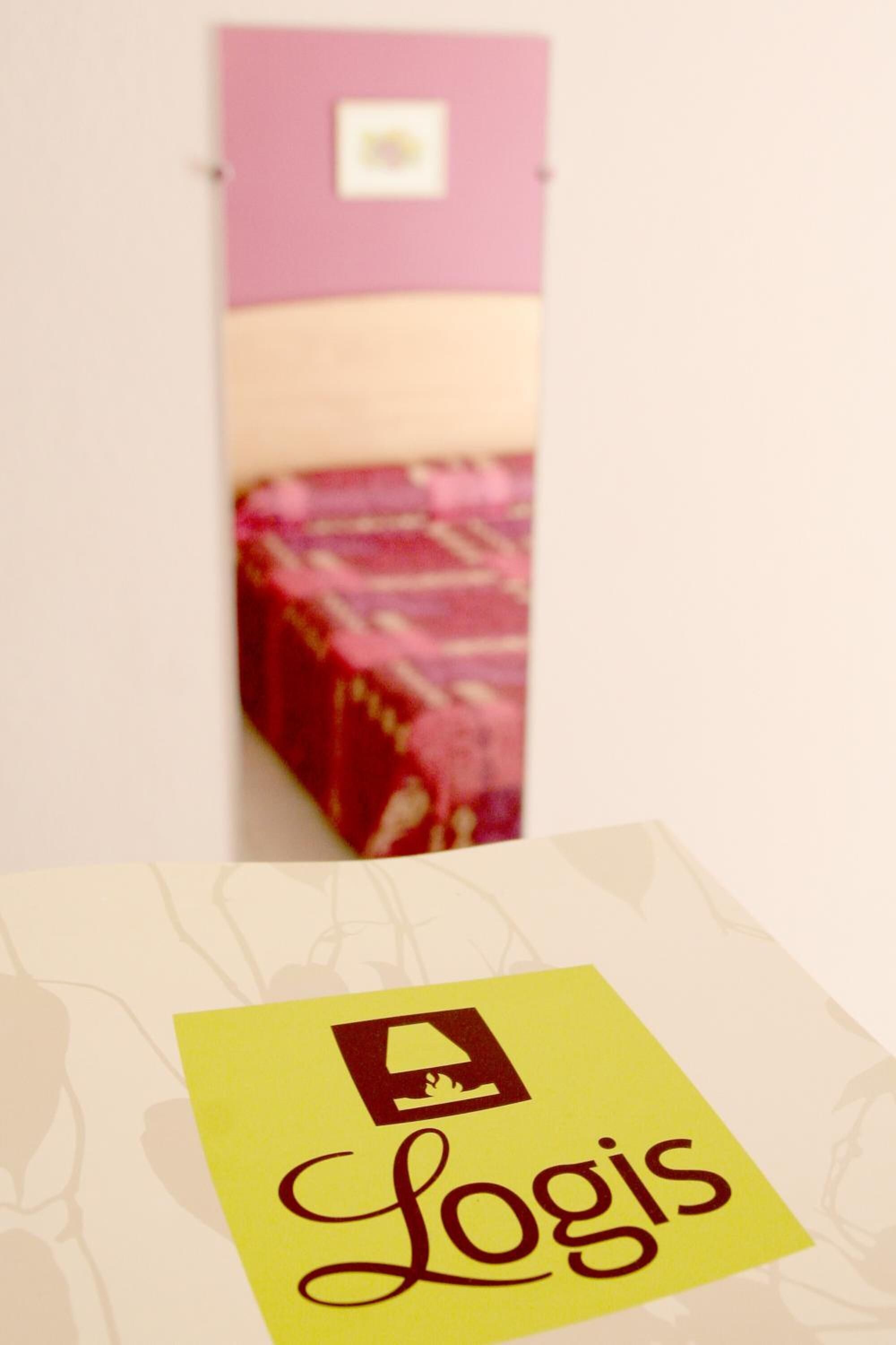 A room with a bed, a pink wall, and a yellow sign with the word "Logis".