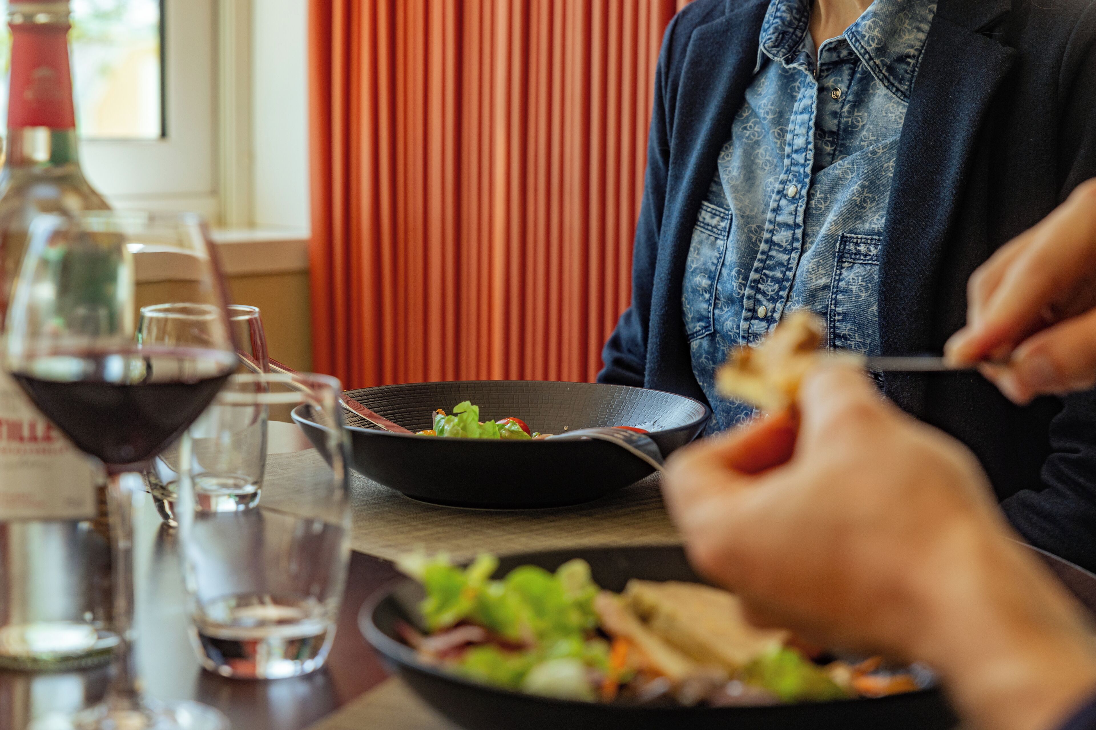 Une table à manger avec une salade, des verres à vin et une bouteille.