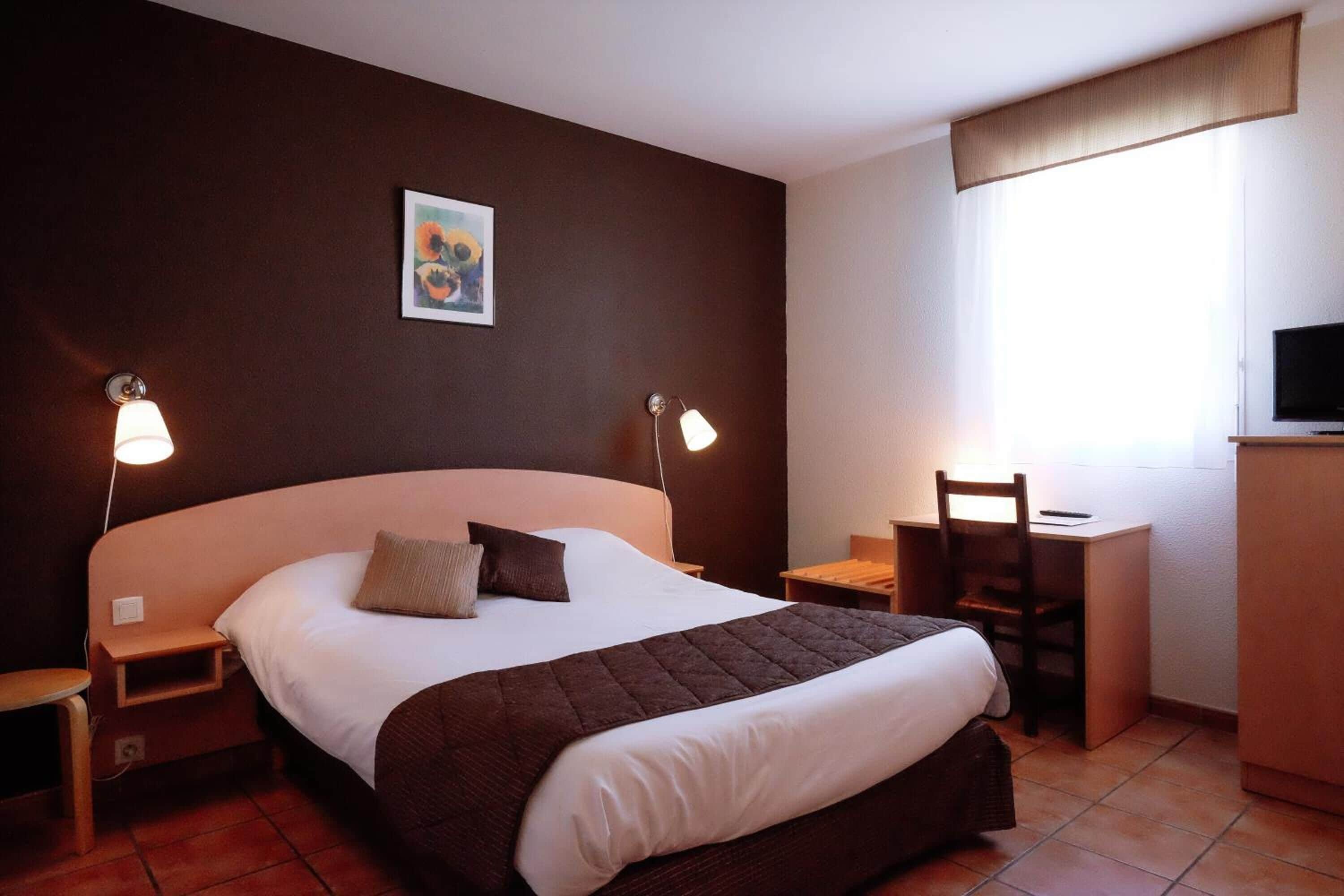 A hotel room with a large bed, bedside tables, a desk, and a television.
