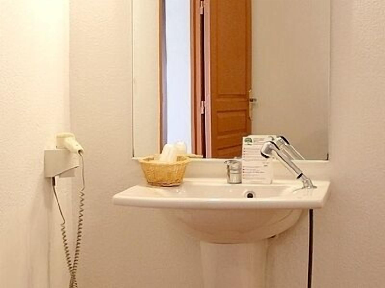 Un baño con lavamanos, espejo, una cesta con artículos de aseo y teléfono.
