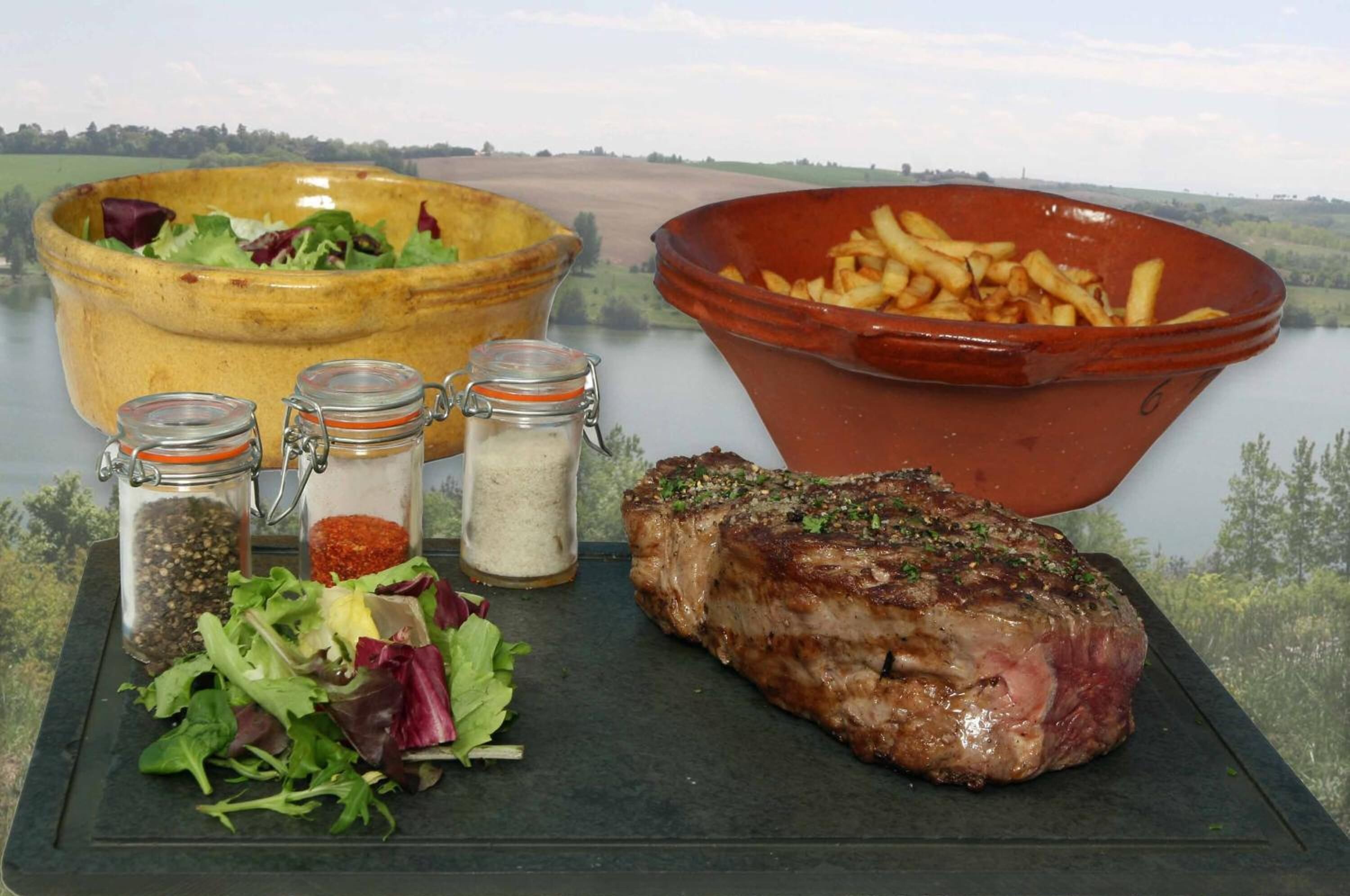 A meal with a steak, salad, and fries on a table with a scenic view.