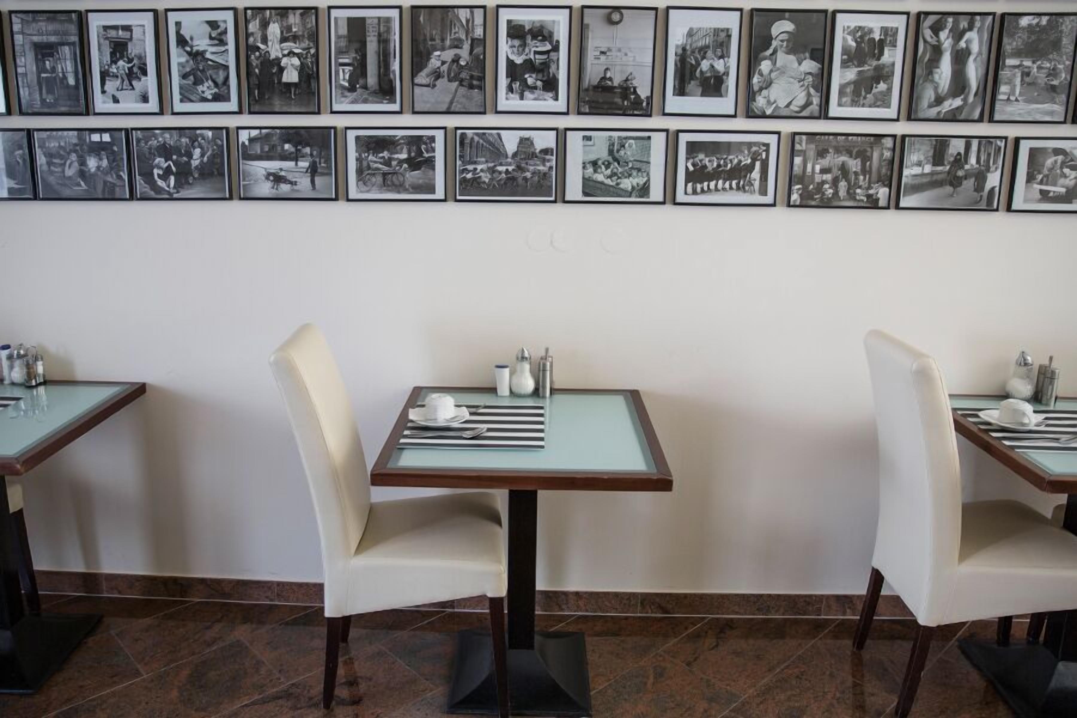 Un restaurant avec deux tables, chacune équipée d’une chaise, d’un plateau en verre et d’une petite table dressée comprenant une tasse, une assiette et des couverts.