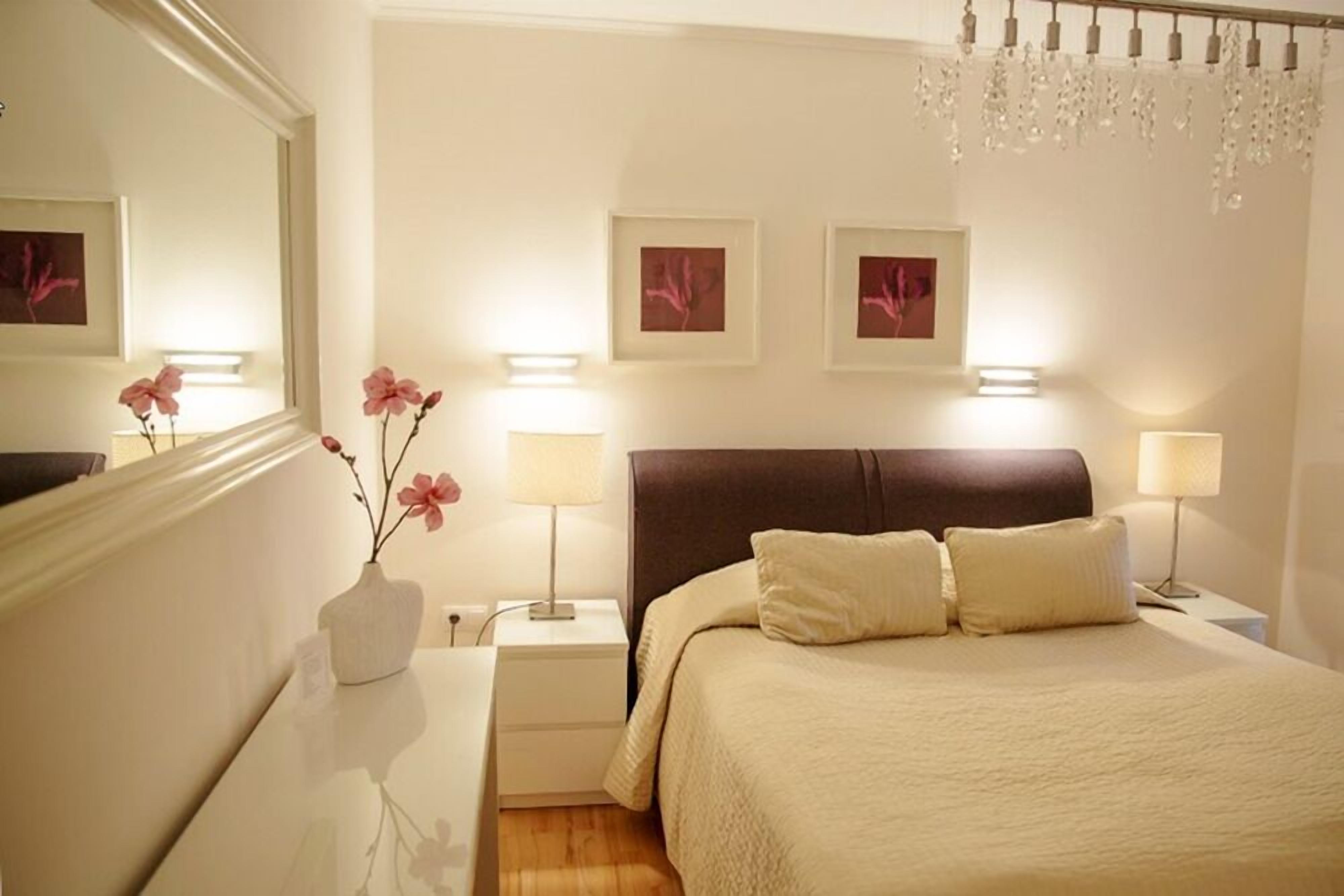 A hotel room with a large bed, two bedside lamps, a nightstand with a vase of flowers, and a chandelier.