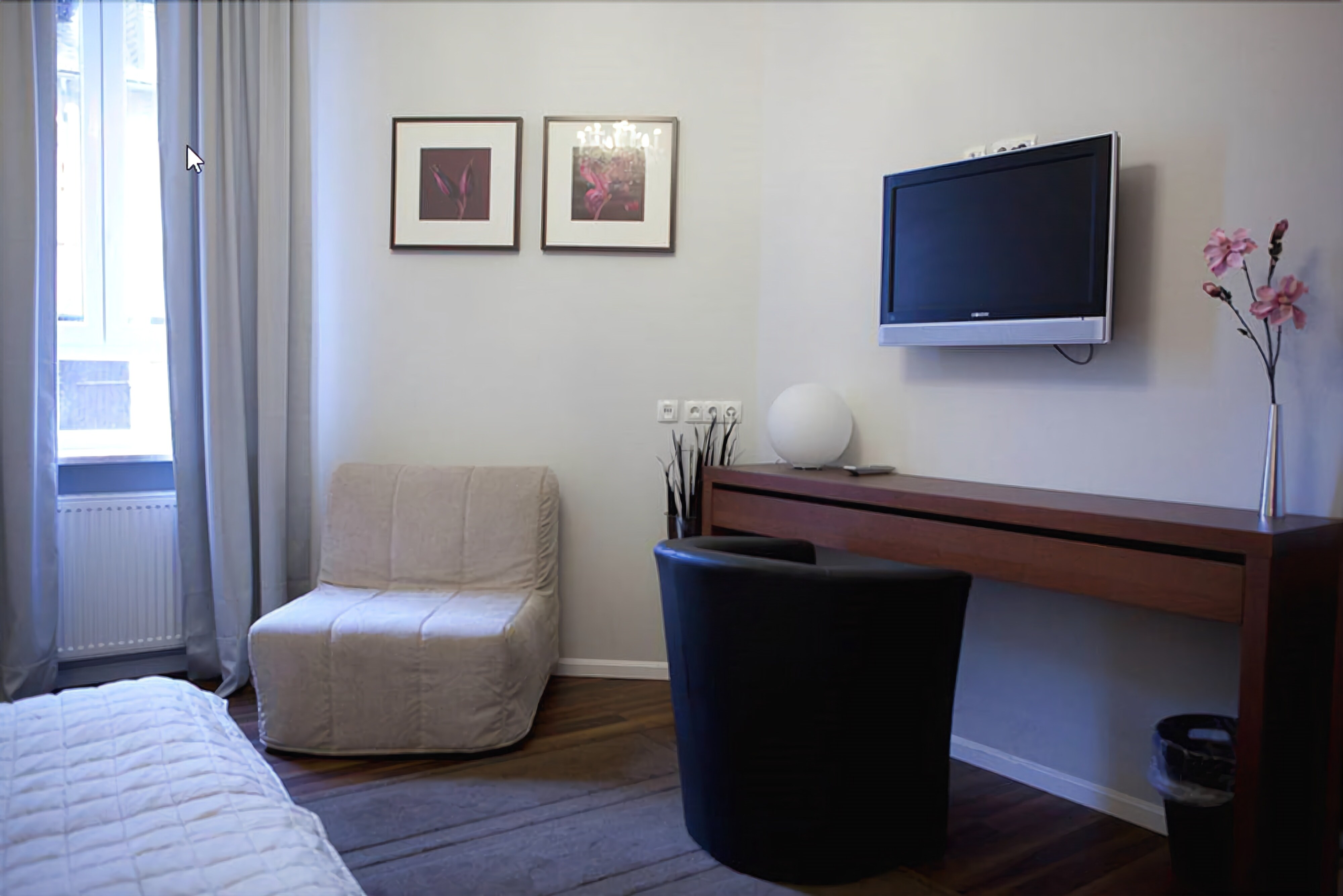 Quarto de hotel com uma cama, escrivaninha com televisão, cadeira e duas quadros na parede.