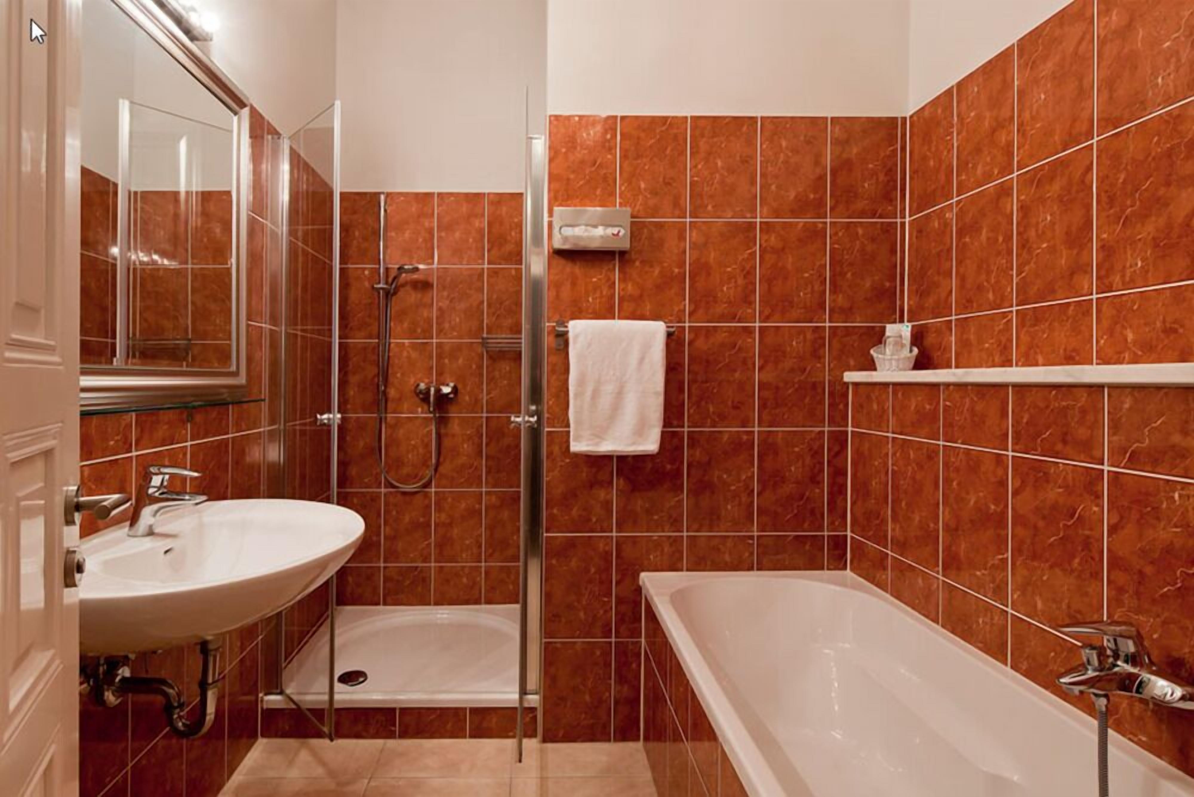 Une salle de bain équipée d’une douche, d’un lavabo et d’une baignoire, avec des murs recouverts de carreaux marron et une serviette blanche.
