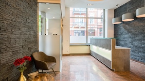 A modern reception area with a stone wall, a reception desk, a chair, and a vase with flowers. - Aurora Hotel (Wiesbaden)
