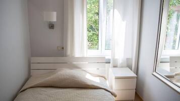 A bedroom with a bed, a nightstand, a wall-mounted lamp, and a window with curtains.