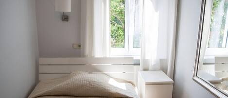 A bedroom with a bed, a nightstand, a wall-mounted lamp, and a window with curtains.