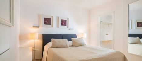 A bedroom with a bed, bedside lamps, a nightstand, a mirror, and framed pictures on the wall.