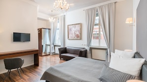 A hotel room with a bed, a desk, a chair, a television, and a chandelier. - Aurora Hotel (Wiesbaden)
