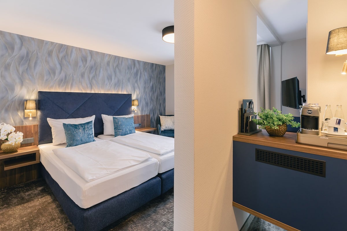 Ein modernes Hotelzimmer mit einem großen Bett, einem Schreibtisch mit Kaffeemaschine und einem Fernseher.