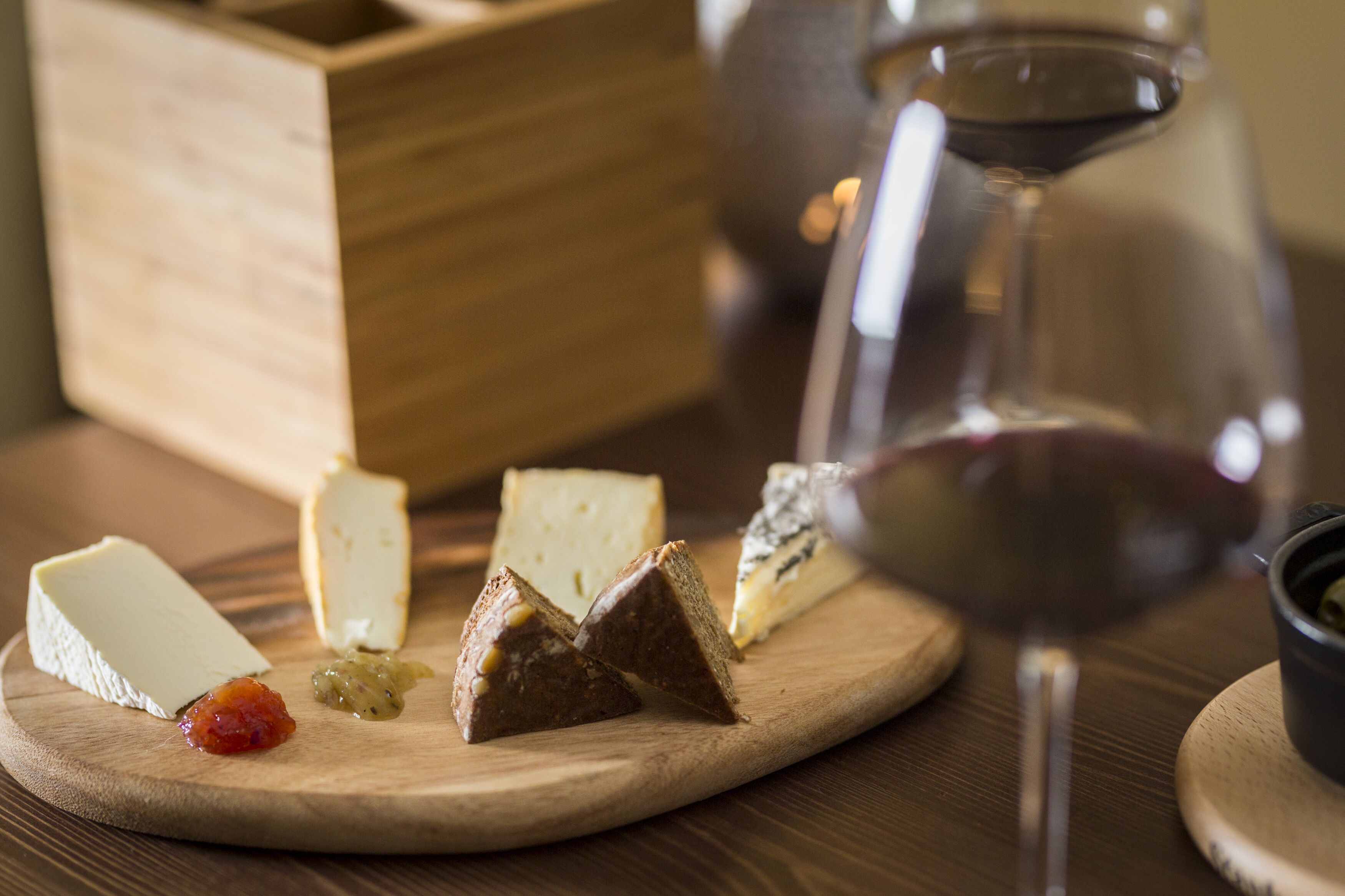 Ein Holzbrett mit verschiedenen Käsesorten, einem Glas Rotwein und einer kleinen Schale Oliven.