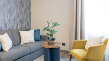 Una sala moderna con un sofá gris, un sillón amarillo y una mesa de centro redonda de madera con una planta en maceta.