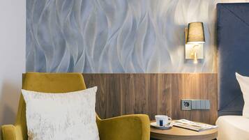 Et hotelværelse med et moderne design, der inkluderer en væg med struktur, en træpanelvæg, en gul lænestol, en hvid pude, et natbord med lampe og et magasin.