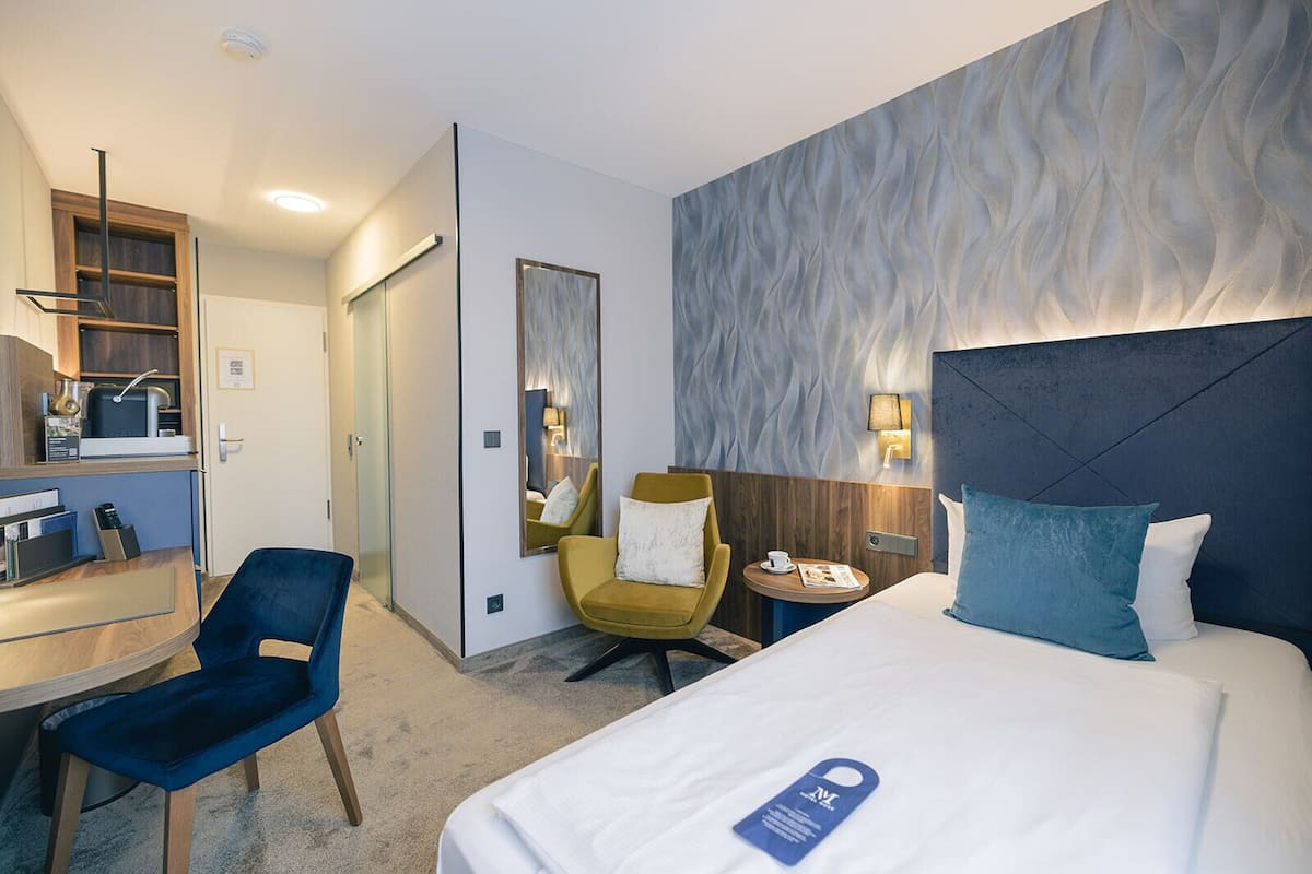 Ein Hotelzimmer mit einem Bett, einem Schreibtisch, einem Stuhl, einem kleinen Tisch und einem Spiegel.