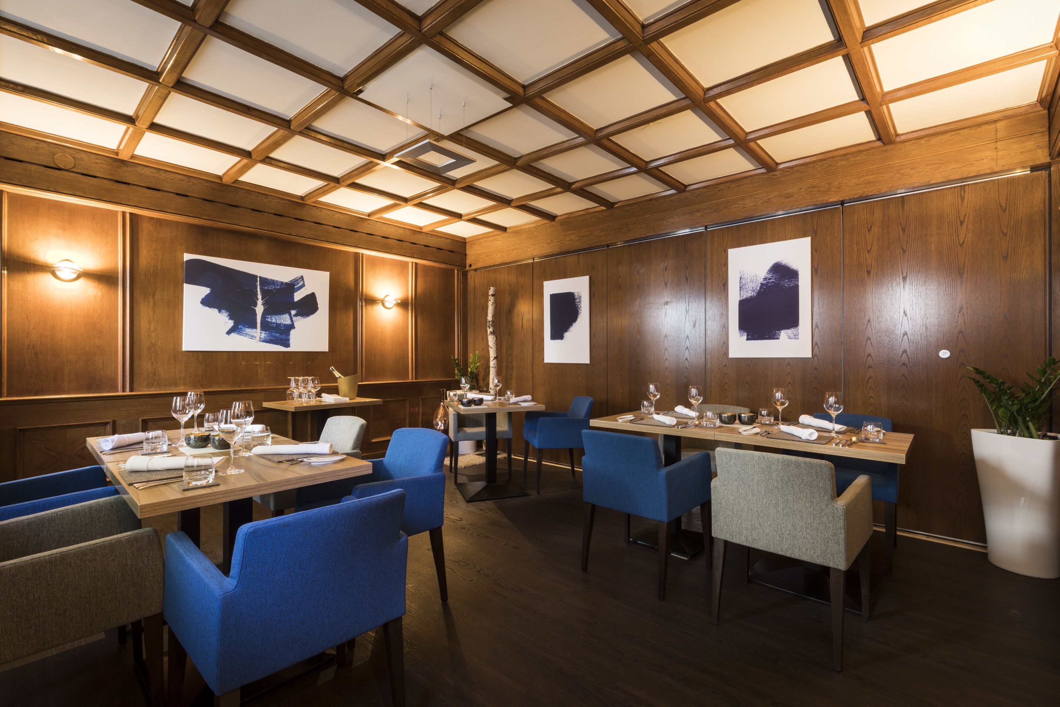 Un restaurante con paneles de madera, sillas azules y mesas dispuestas para comer.