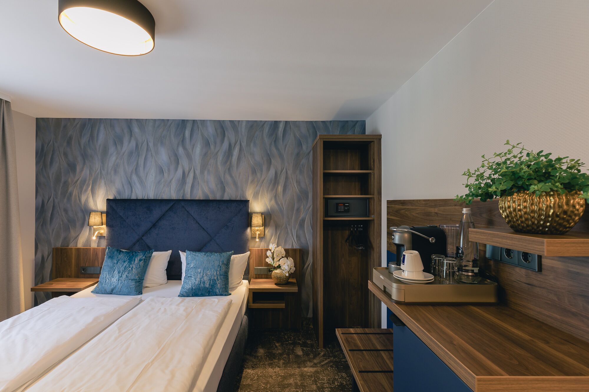 Quarto moderno com cama, mesas de cabeceira, um criado-mudo, prateleira embutida e luminária de parede.