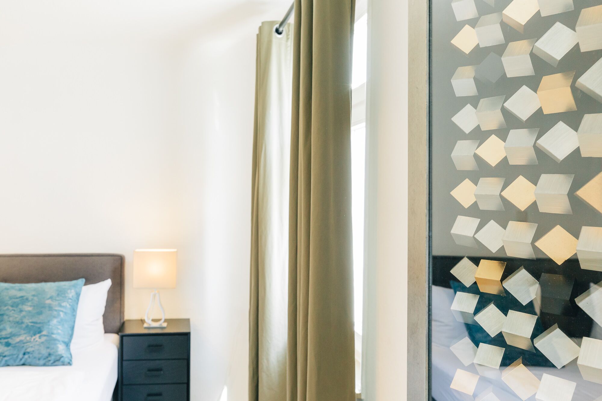 Una habitación de hotel con una cama, una mesita de noche con lámpara y una ventana con cortinas de diseño geométrico.