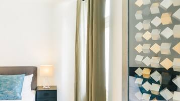 Una habitación de hotel con una cama, una mesita de noche con lámpara y una ventana con cortinas de diseño geométrico.
