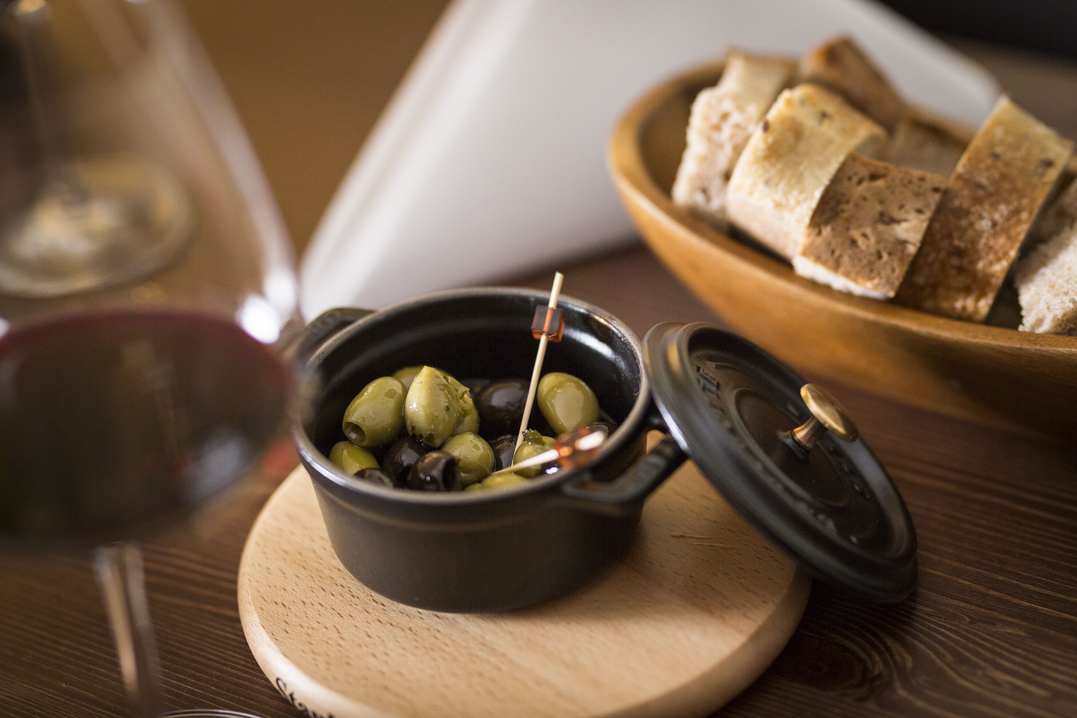 Eine Schale Oliven, ein Holzservierbrett, ein Glas Rotwein und eine Brotteller.