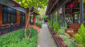 A narrow pathway flanked by potted plants and wooden furniture, leading to a covered area with a tiled roof. - Betel Garden Villas (Da Nang)