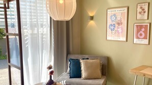 A modern living room with a sofa, a small table, and two hanging lamps. There are framed pictures on the wall and a window with curtains. - Hotel-Bistro-Europa (Merchweiler)