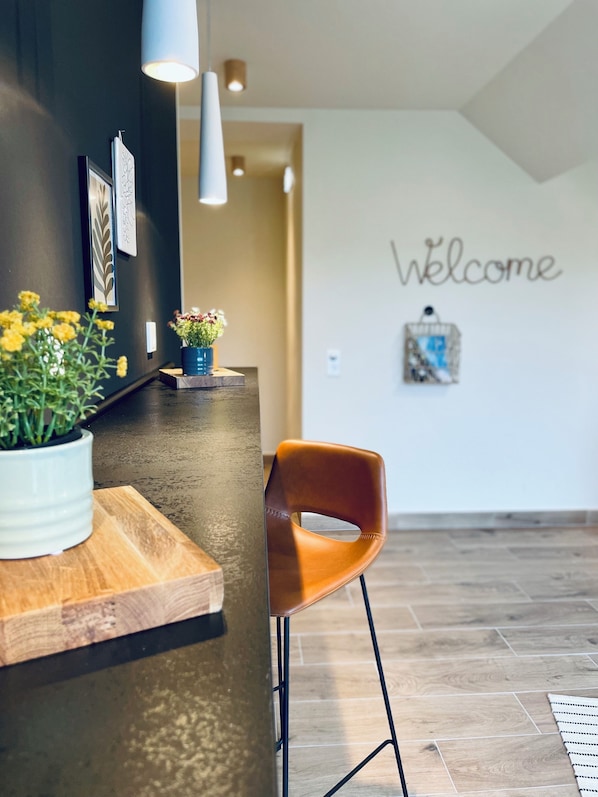 Una zona de recepción con un mostrador de madera, una planta en maceta y un letrero que dice 'Welcome' en la pared.