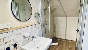 A bathroom with a white sink, a round mirror, a shower, and a tiled wall.
