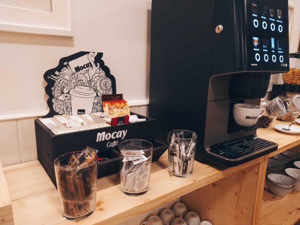 A Mocay coffee station with a coffee machine, cups, and a display of coffee pods.
