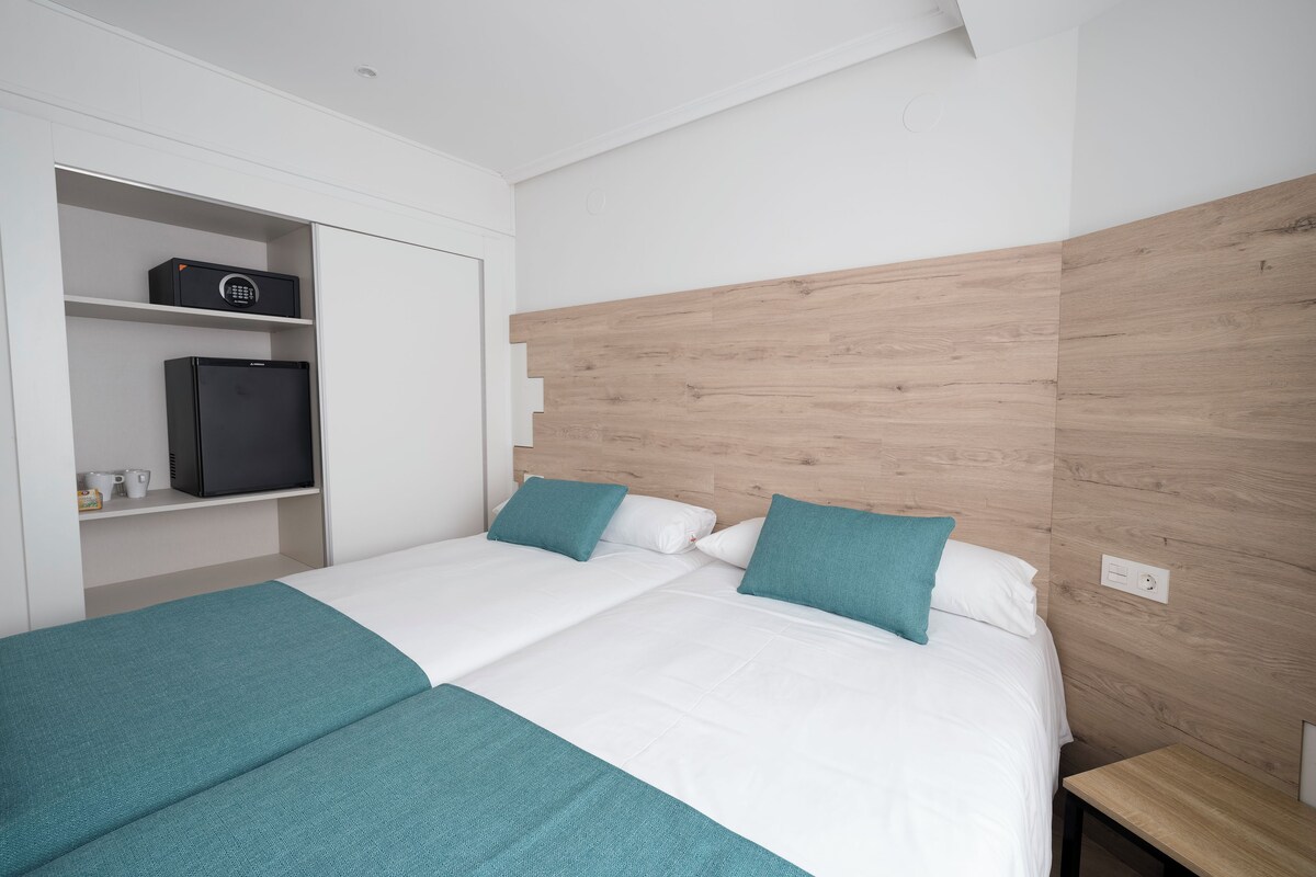 A modern hotel room with a bed, a wardrobe, and a small kitchenette.