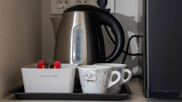Een kitchenette met een waterkoker, een dienblad met mokken en een beker, en een stopcontact met drie aansluitingen.