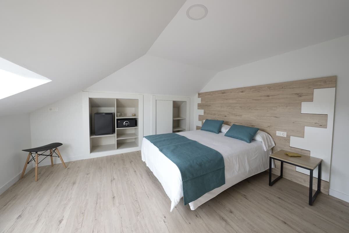 Une chambre moderne avec un plafond en pente, une armoire intégrée, un lit avec une tête de lit en bois et une petite table.