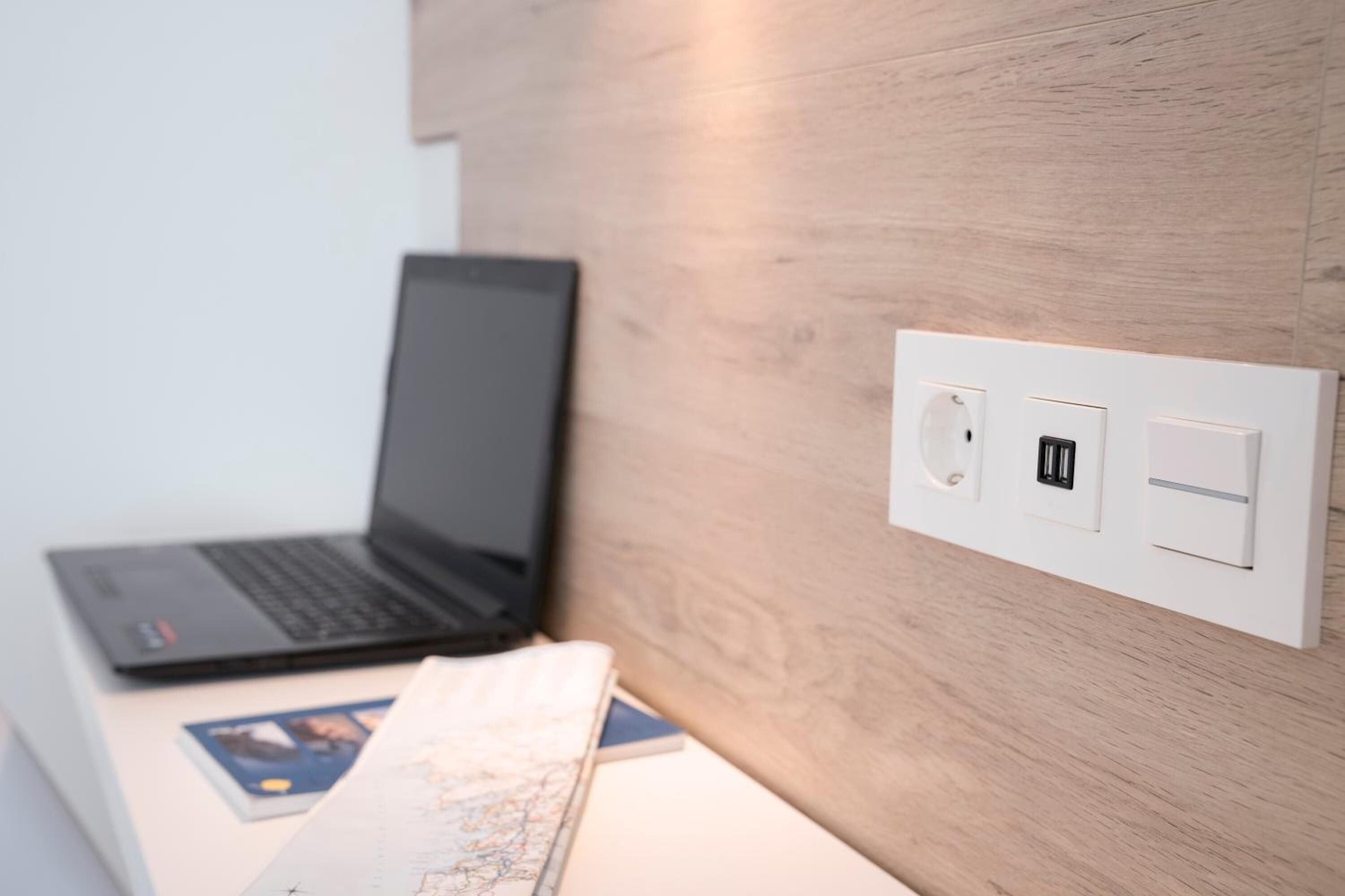 A laptop on a desk with a map and a book, a wall socket, and a USB port.