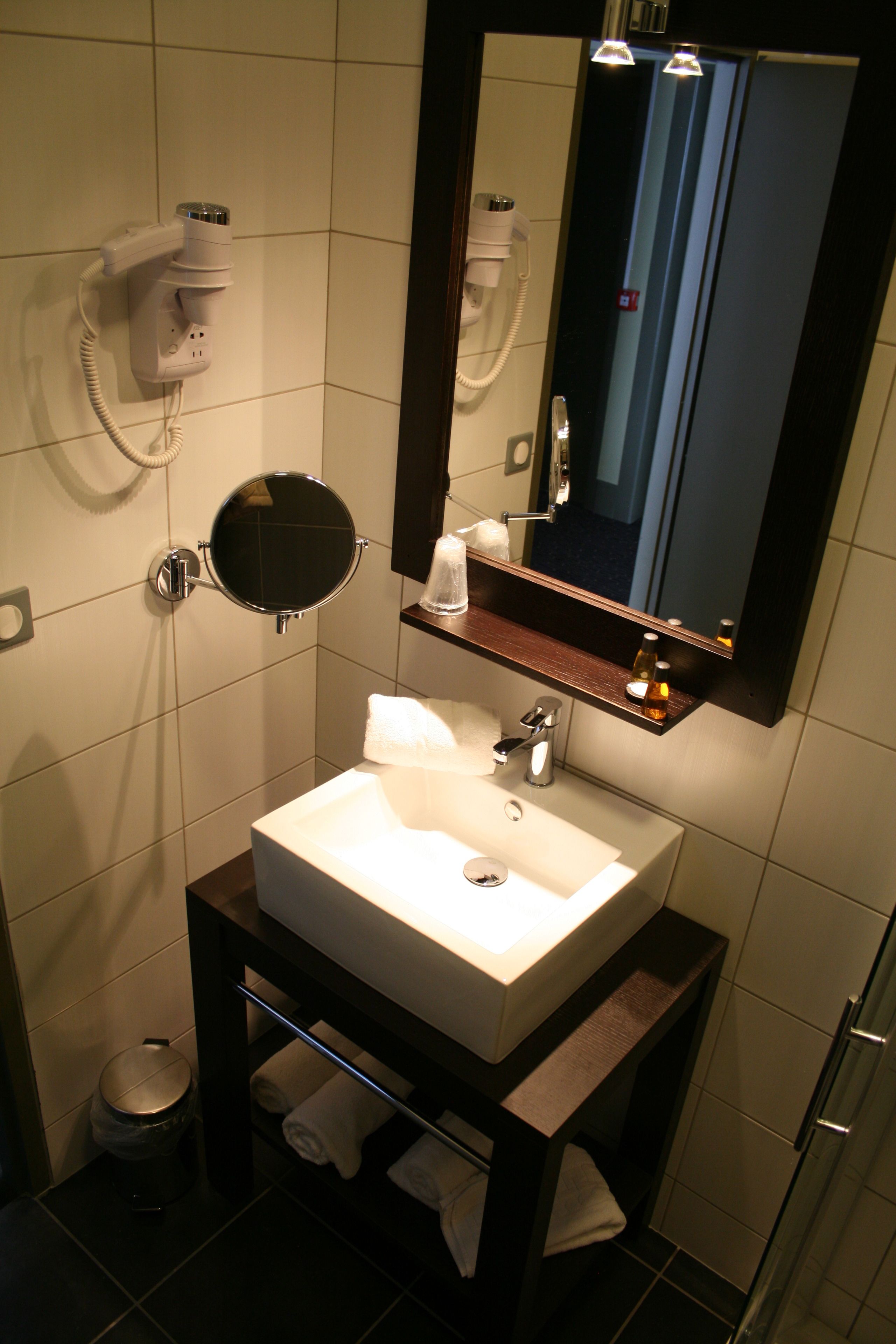 A bathroom with a white sink, a round mirror, a towel rack, and a hairdryer.