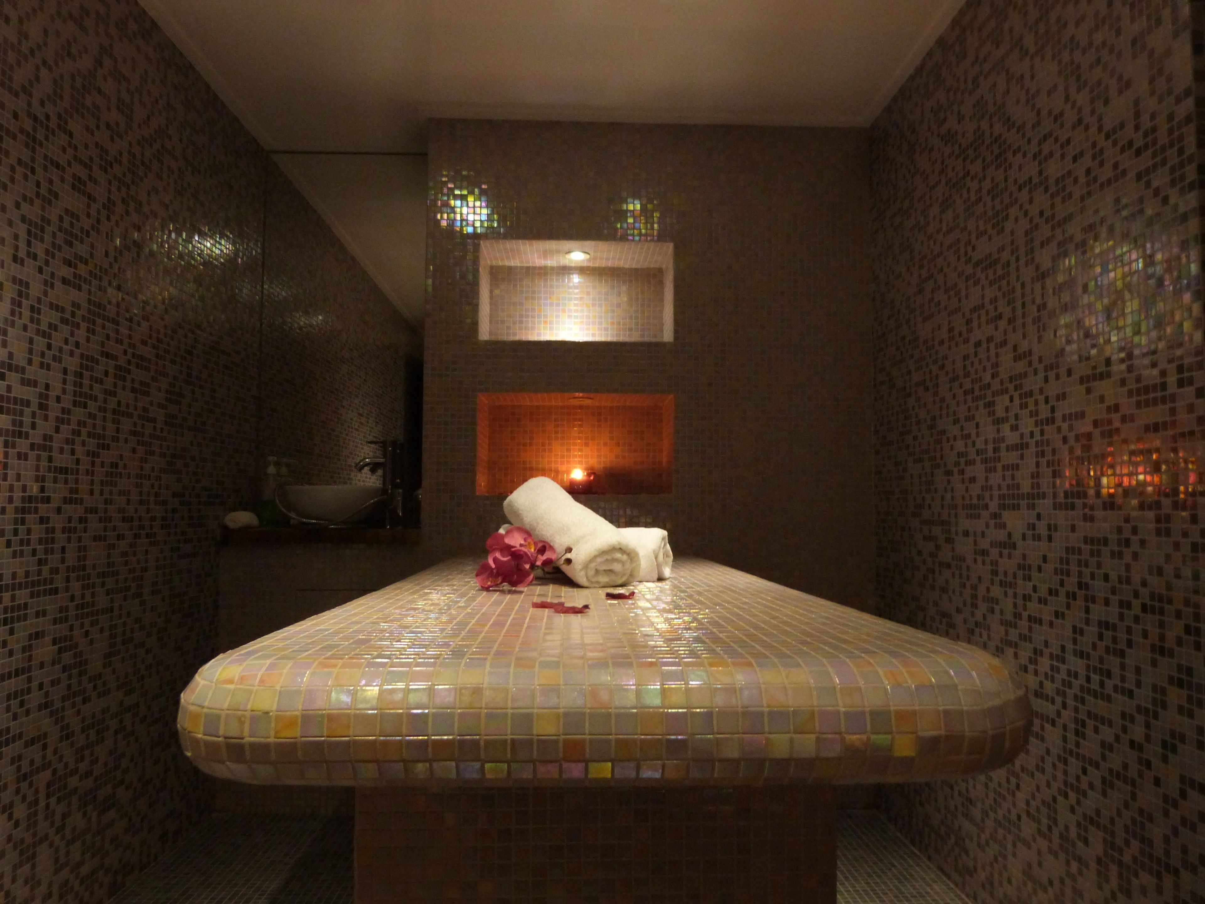 A bathroom with mosaic tile walls, a sink, a mirror, and a towel on the counter.