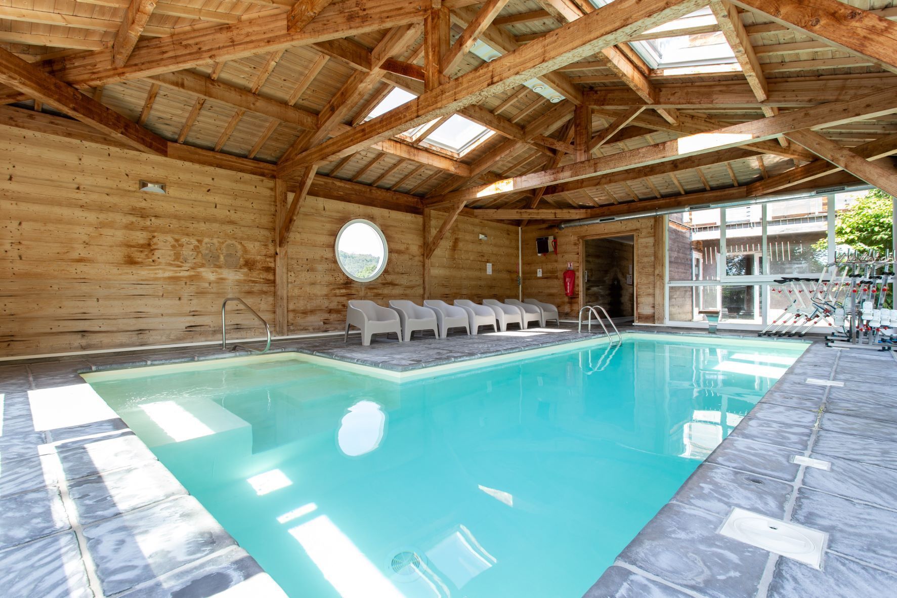 A wooden cabin with a swimming pool, wooden beams, and a circular window.