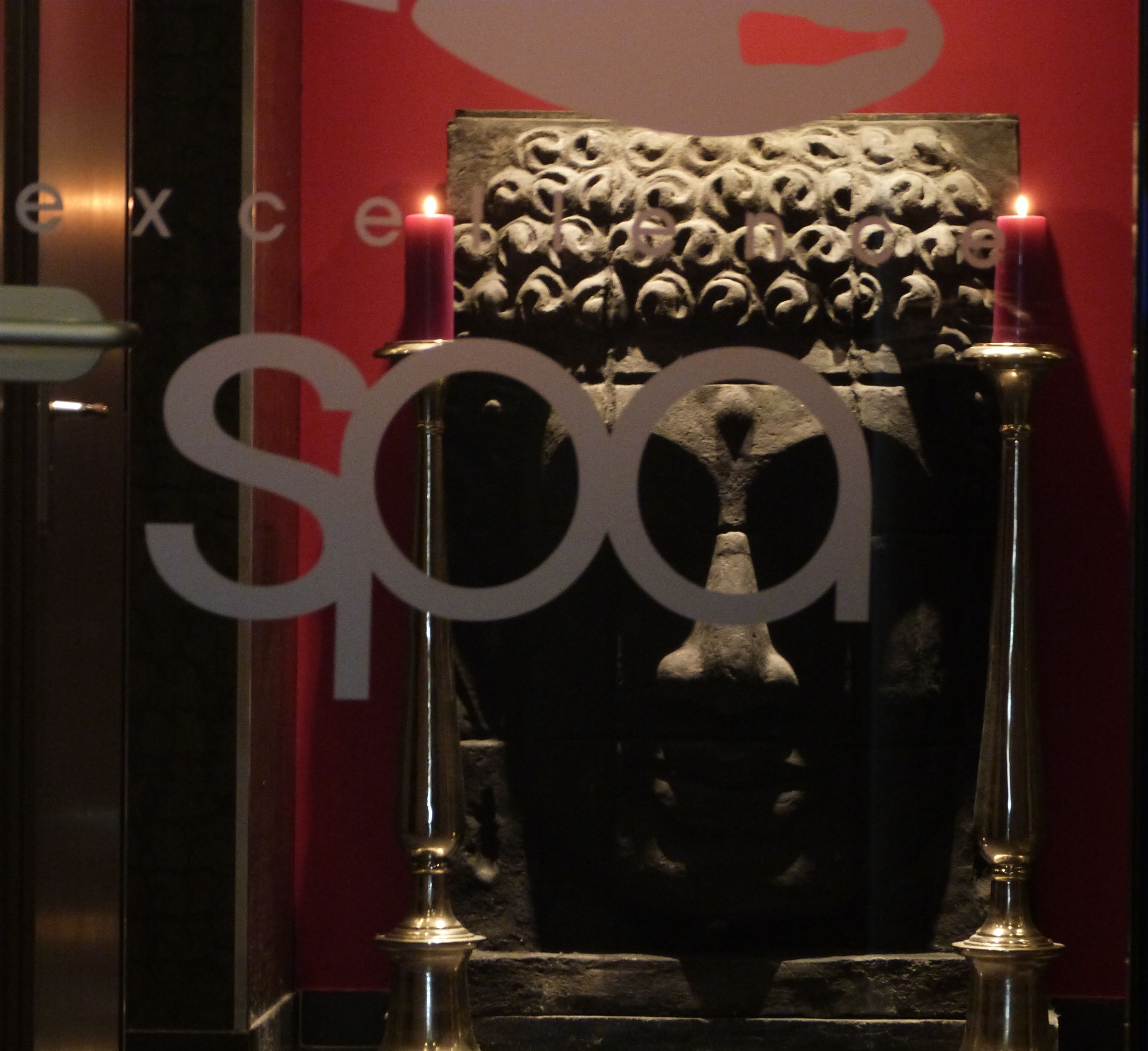 A room with a large, ornate chair and two candles on stands.