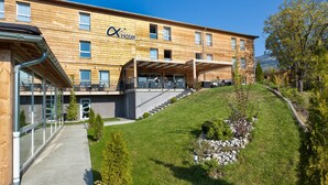 A hotel with a wooden facade, a covered outdoor seating area, and a hillside garden. - Ax'Hotel (Chorges)