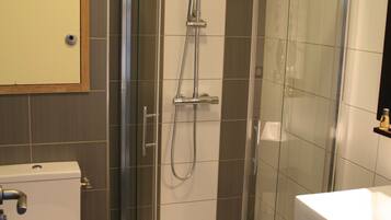 Un baño moderno con ducha de vidrio, inodoro y lavamanos con espejo arriba.