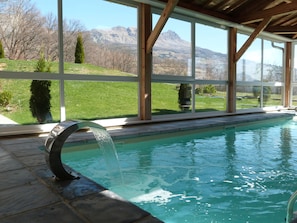 A swimming pool with a waterfall feature, large windows offering mountain views, and a wooden deck.