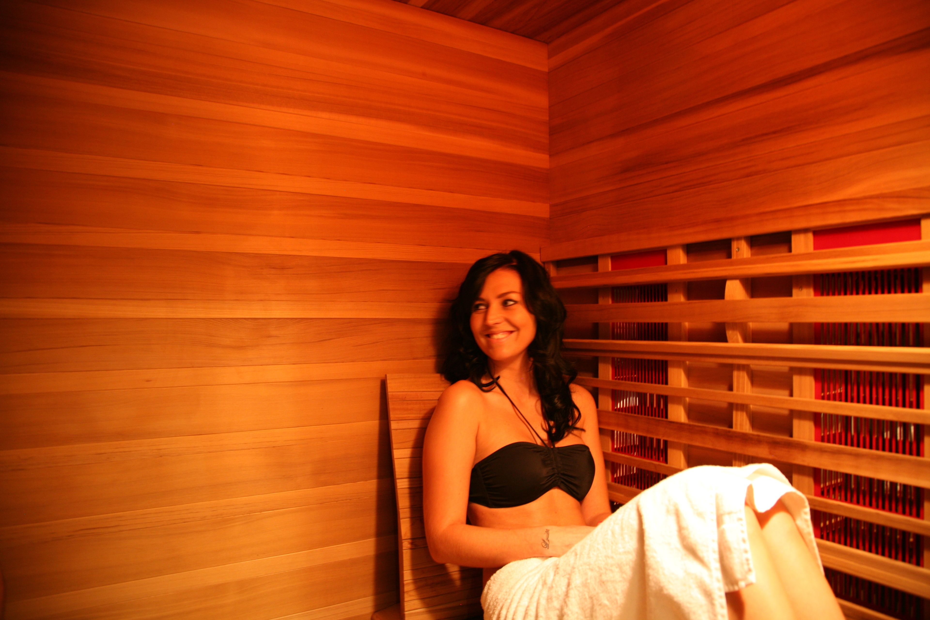 Una persona sentada en una sauna de madera con estantes llenos de botellas.
