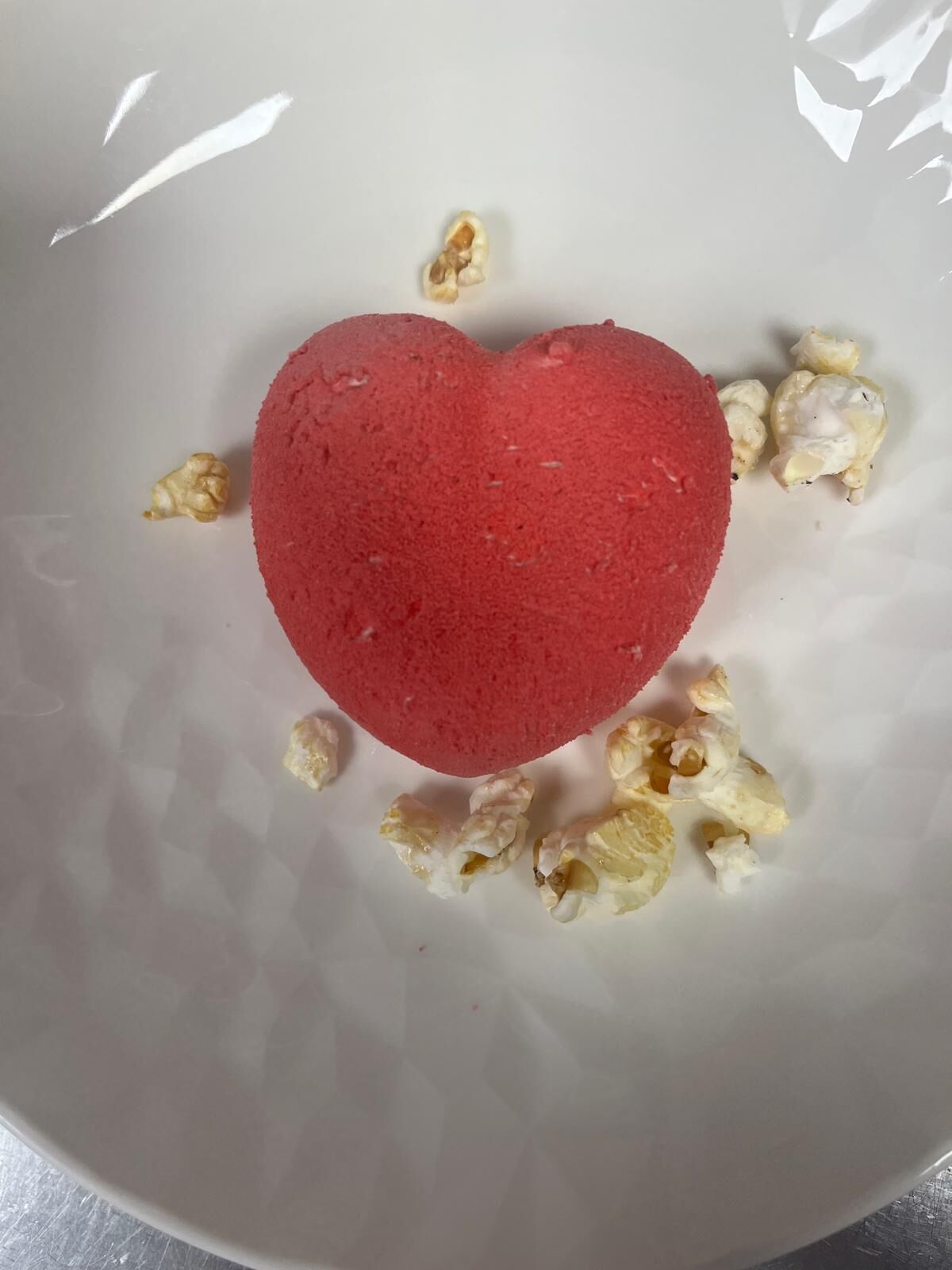 Un postre con forma de corazón sobre un plato con palomitas esparcidas.