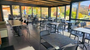 An indoor dining area with tables and chairs, large windows, and a view of the outdoors. - Ax'Hotel (Chorges)