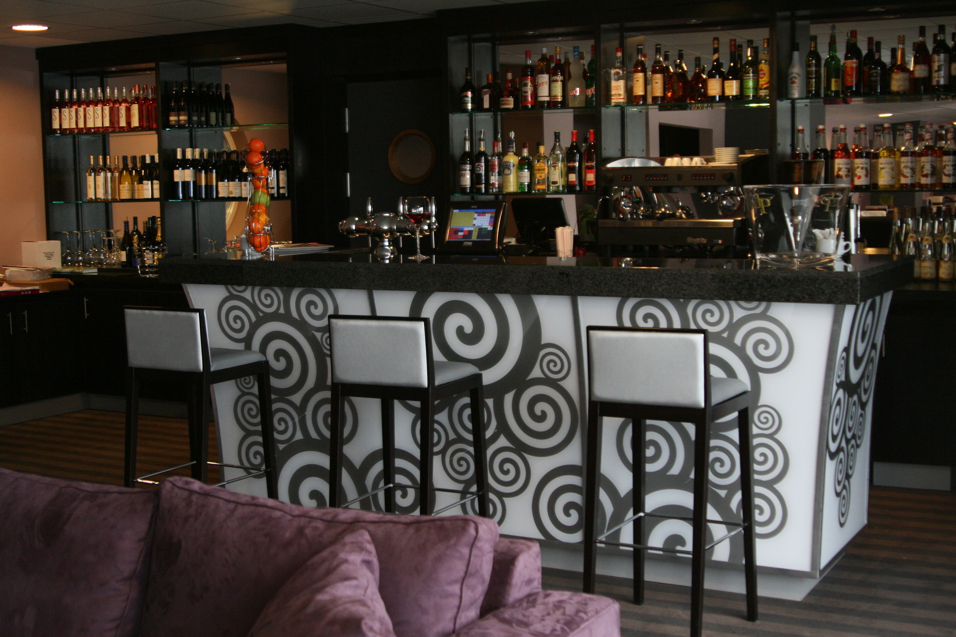 A bar area with a counter, bar stools, and a variety of bottles and glasses.
