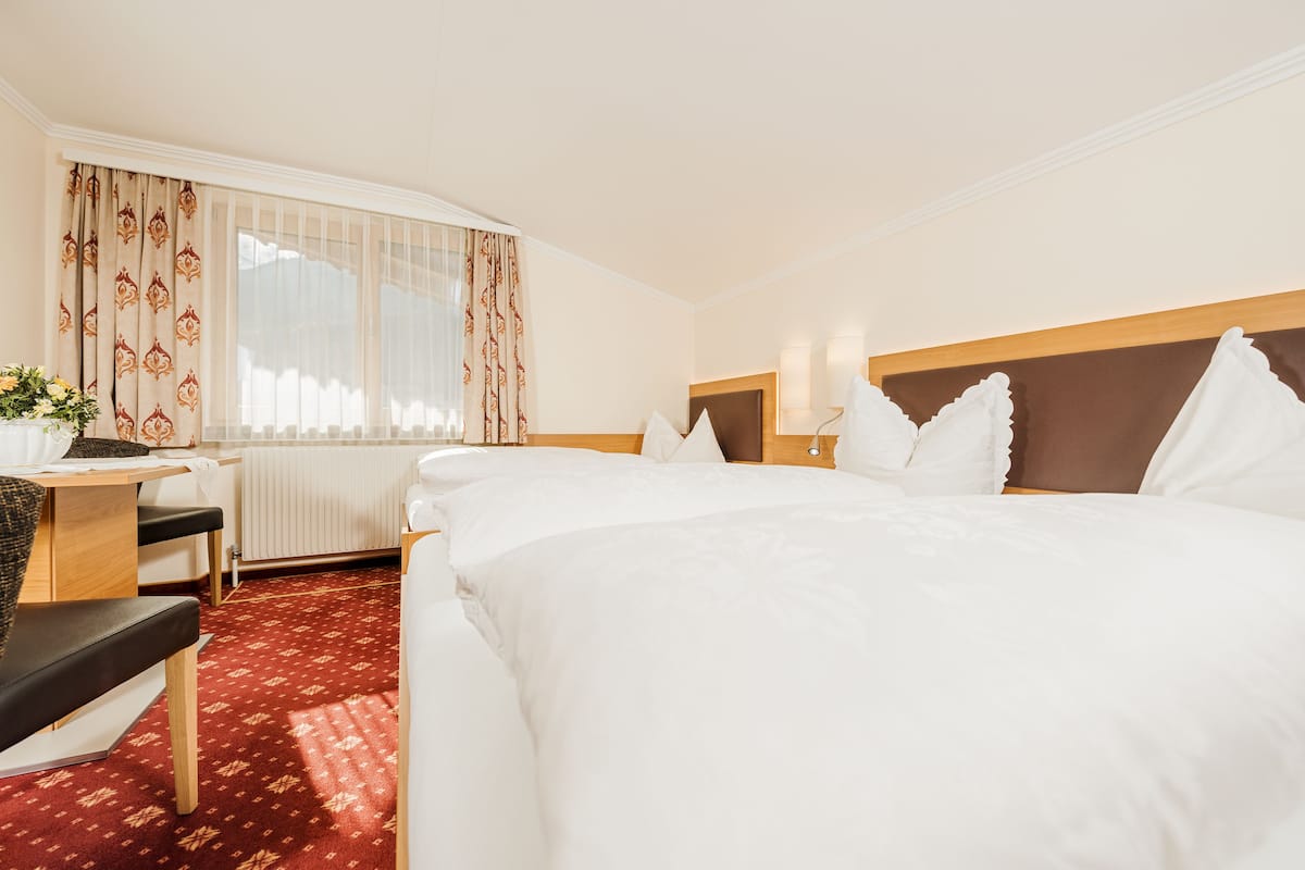 Habitación de hotel con una cama grande, un escritorio con silla, un radiador y una ventana con cortinas.
