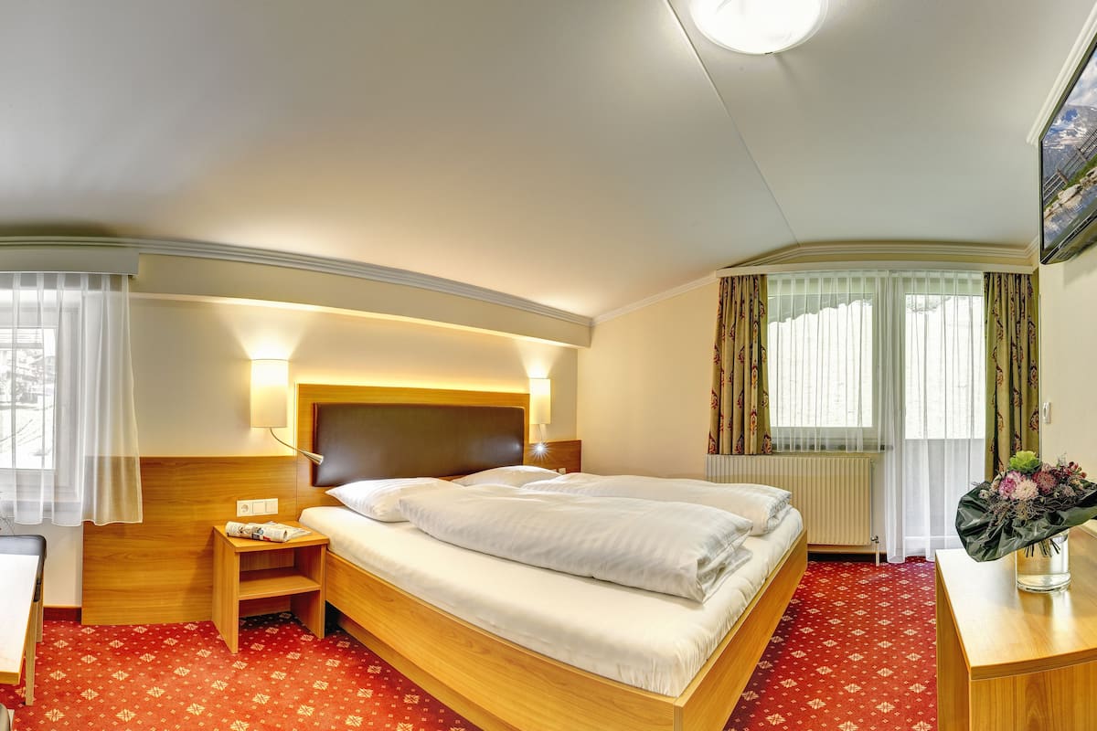 Una habitación de hotel con cama, mesita de noche, lámpara y ventana con cortinas.