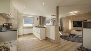 Een moderne keuken met houten vloeren, witte kasten, een inbouwoven en een groot raam dat voor natuurlijk licht zorgt.